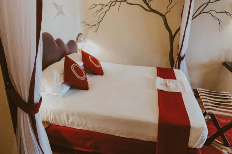 A large bed with red cushions between two white curtains, in front of a tree painted on the wall