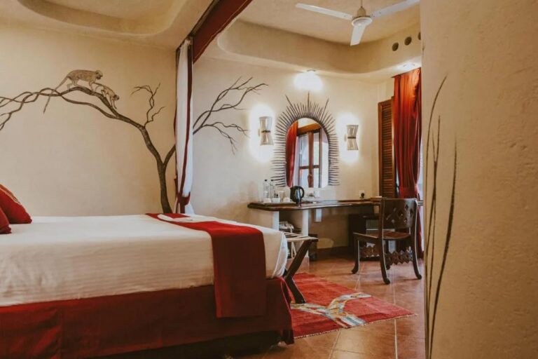 A room with a tree and two monkeys painted on the wall, and a desk under a sunburst mirror