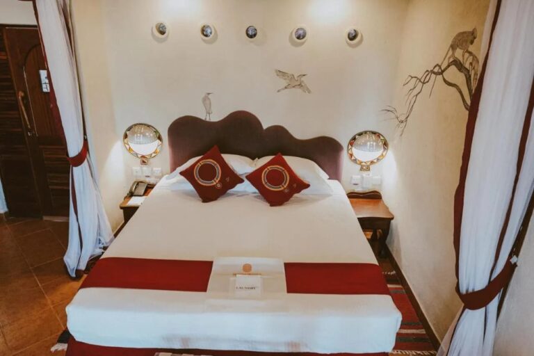 A large bed with a wavy headboard, between two white curtains tied back with red