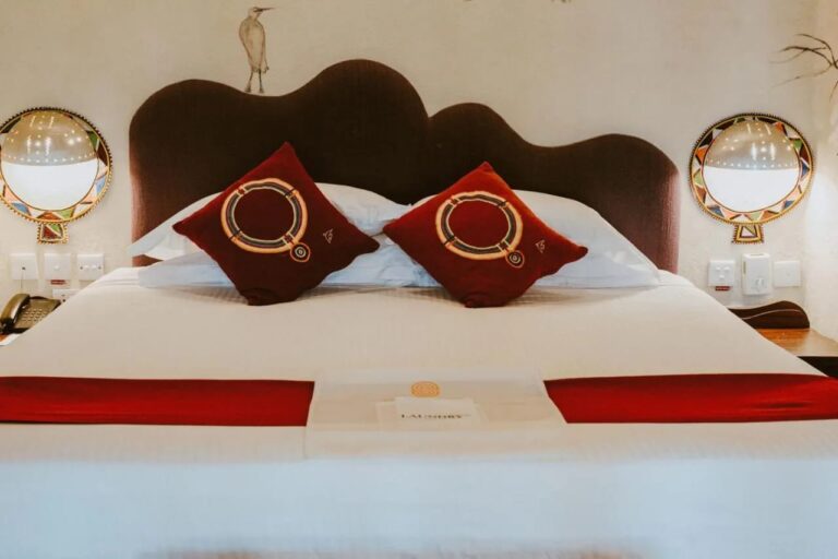 Two embroidered red cushions on a large bed, under a heron painted on the wall and between two colorful wall lights