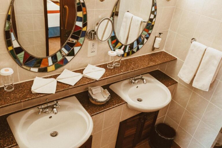 Two sinks on a granite counter, under oval mirrors framed in colorful mosaic