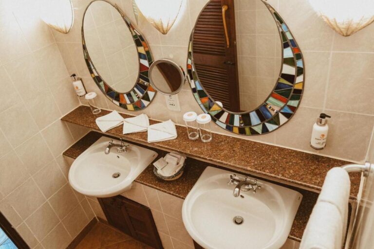 A bathroom with two sinks and a magnifying mirror between two mosaic mirrors