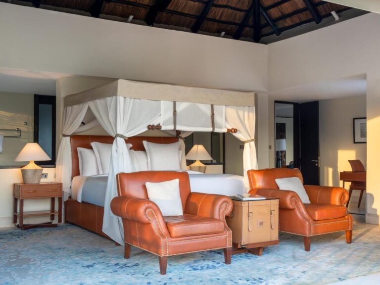 A room with a four-poster bed and two orange leather armchairs