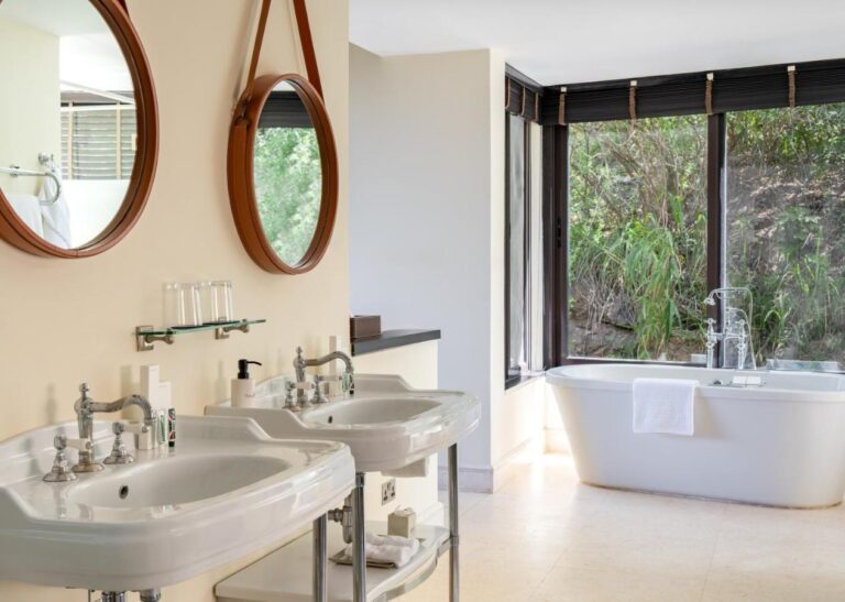 A bathroom with two freestanding washbasins, round mirrors and a bathtub in front of a picture window
