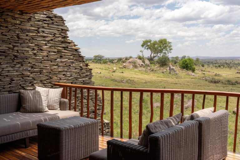 A terrace with woven armchairs, between a stacked-stone wall and the rock-strewn savanna