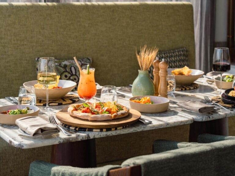 A pizza, salads, a cocktail and two glasses of wine on a marble table