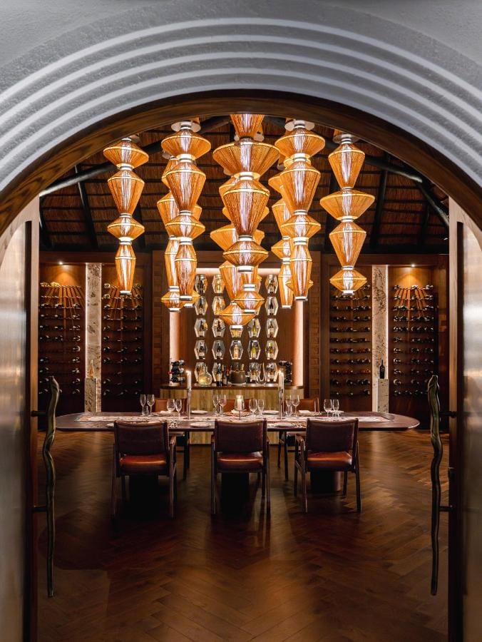 The wine cellar, with a long table set under woven pendant lights, seen through an arch