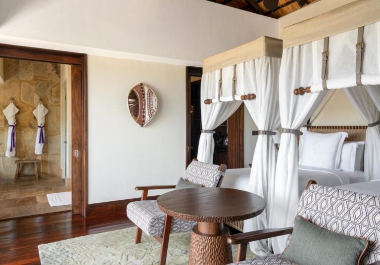 A room with two four-poster beds, a painted shield on the wall and the stone bathroom at the back