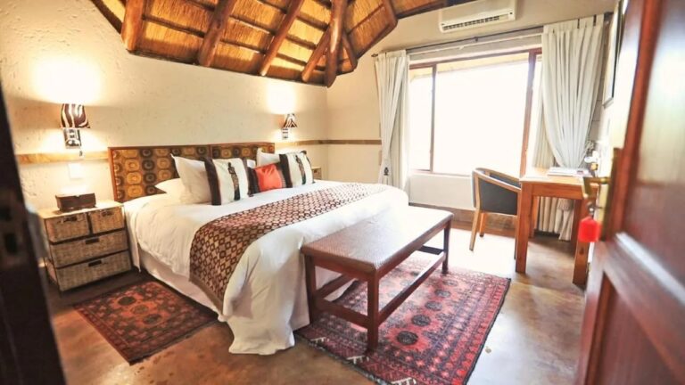 A room under thatched roof timbers, with a double bed, a wooden bench and red rugs
