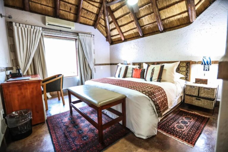 A room under the thatch, with an air conditioner, a wooden desk and a bench at the foot of the bed