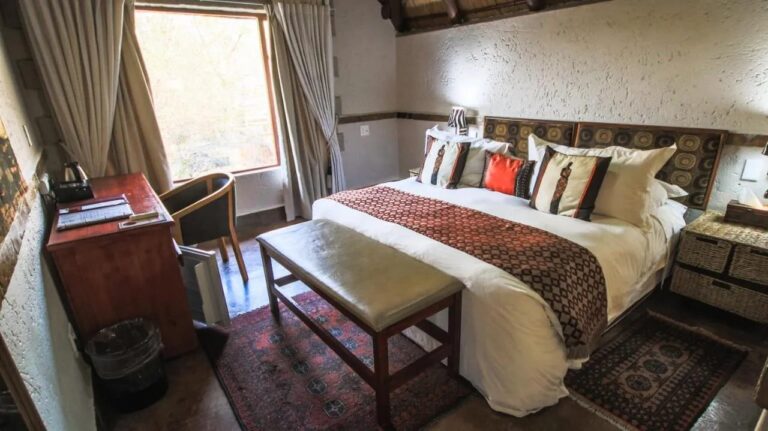 A room with a double bed, a desk under the window and a padded bench