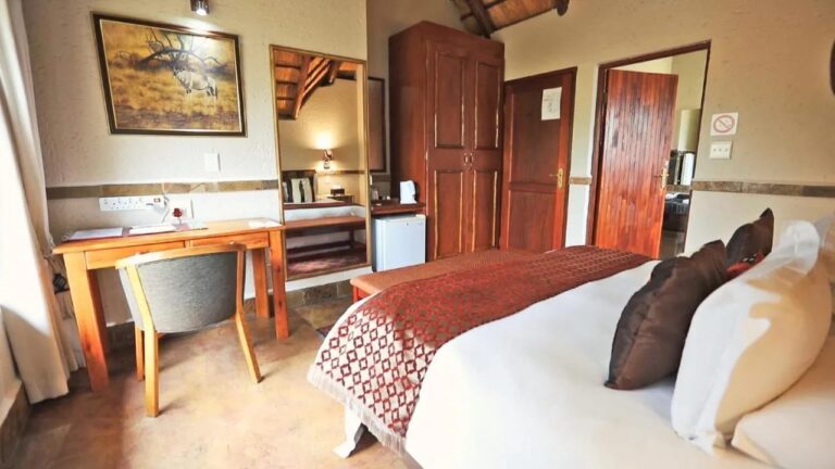 A room with a desk, a wooden wardrobe, a small fridge and a painting of an oryx on the wall
