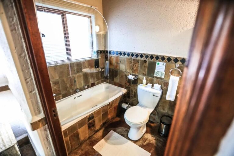 A bathroom with a bathtub and a toilet, its walls tiled in stone
