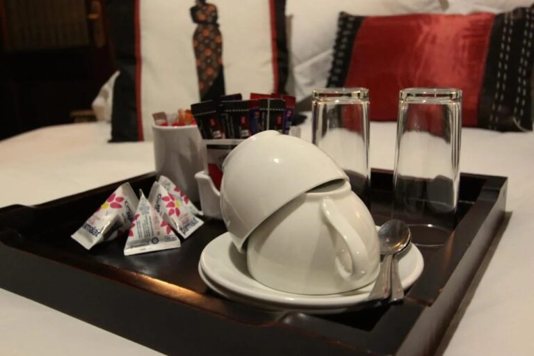 A tray with cups, glasses and packets of tea and coffee, set on a bed