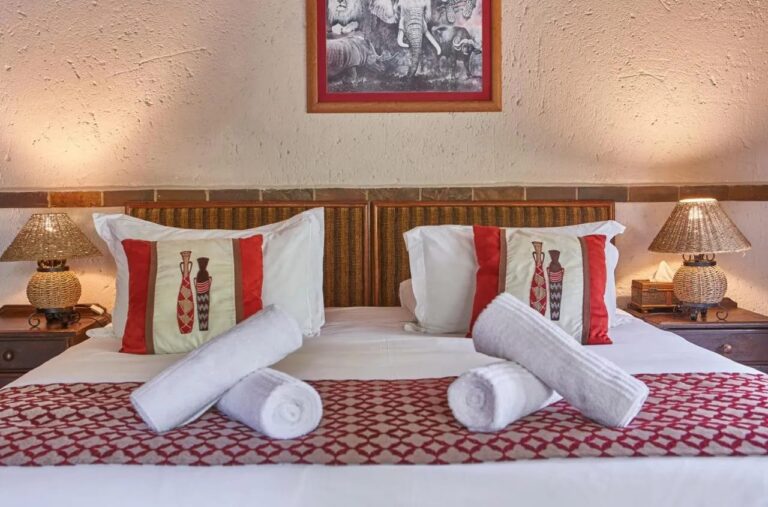 A double bed with rolled towels, under a black-and-white picture of a lion, an elephant, a rhino and a buffalo