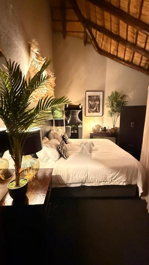 A room under thatched roof timbers, with a white double bed, potted palms and a black-and-white photo on the wall