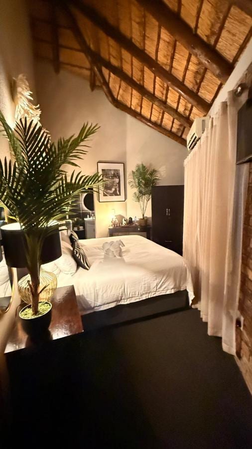 A room under the thatch, with a double bed, a dark wardrobe and sheer curtains at the window
