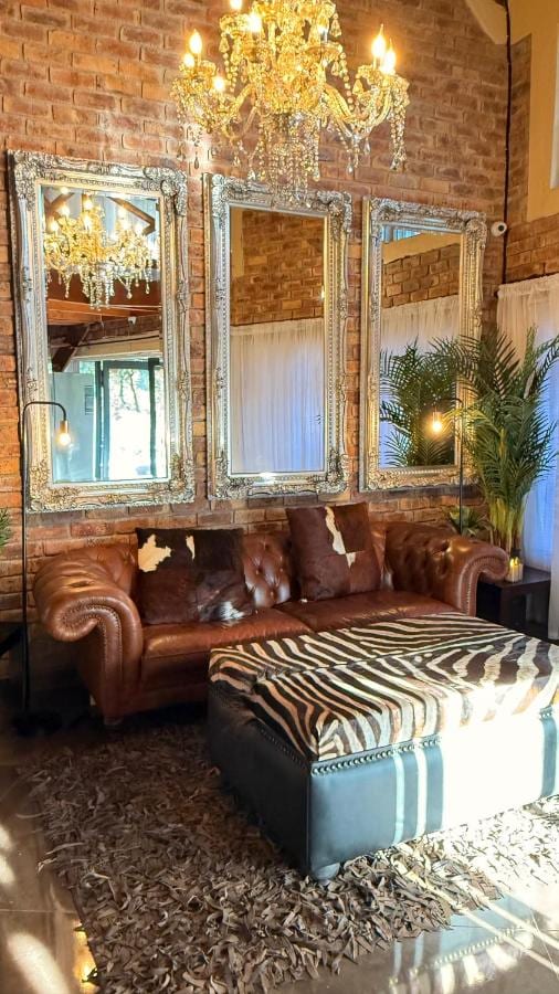 A leather Chesterfield sofa and a zebra-print ottoman under a crystal chandelier, in front of three large mirrors and a brick wall