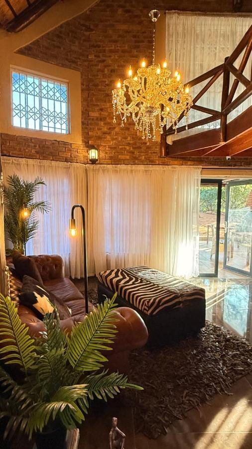 The lounge under high roof timbers, with a chandelier, a leather sofa, a zebra-print ottoman and a wooden mezzanine