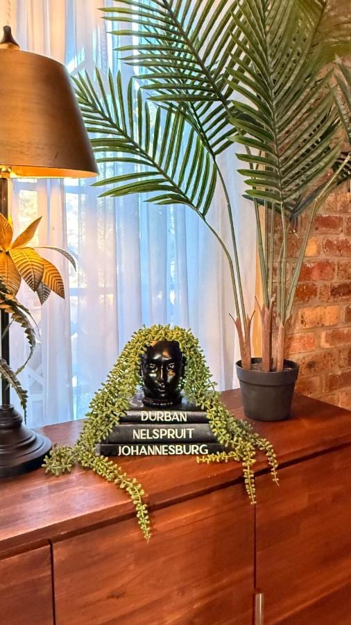 A black bust resting on three books, framed by a trailing plant, on a wooden cabinet near a palm