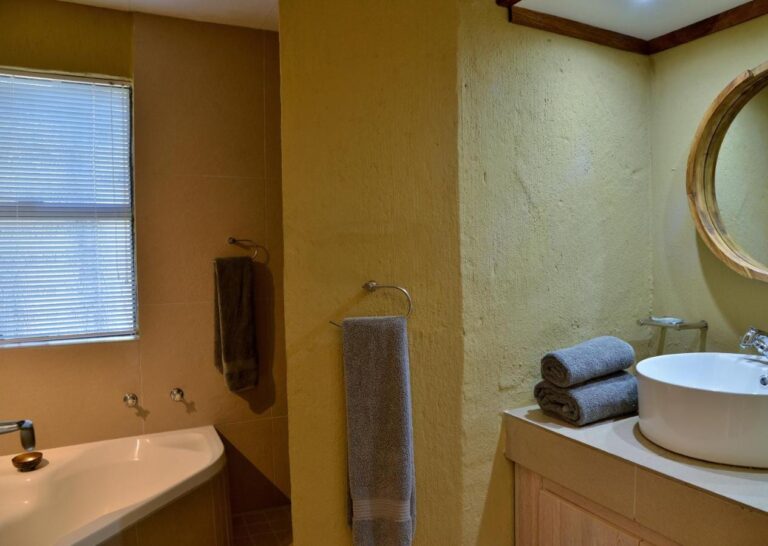 A bathroom with a bathtub, a round vessel sink and a round wood-framed mirror
