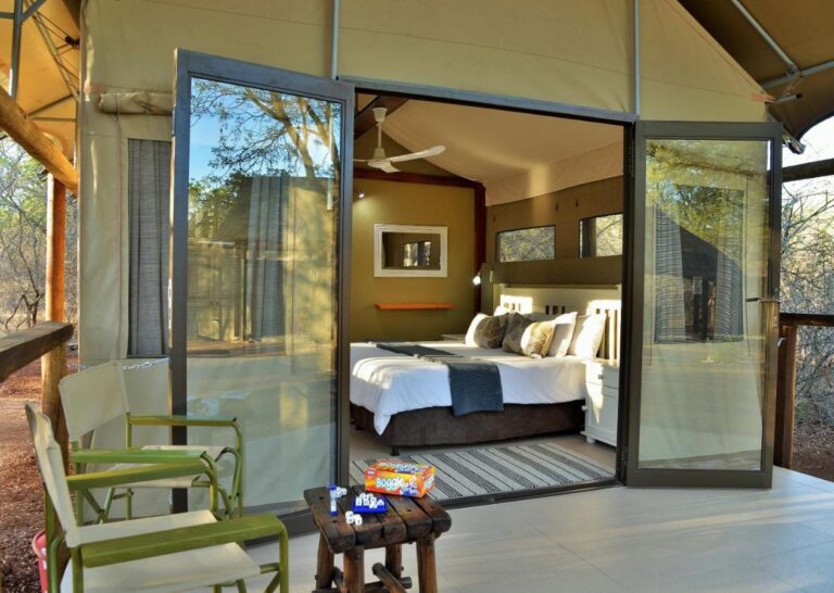 A tent seen from its deck, glass doors open onto the bed, with green armchairs in front