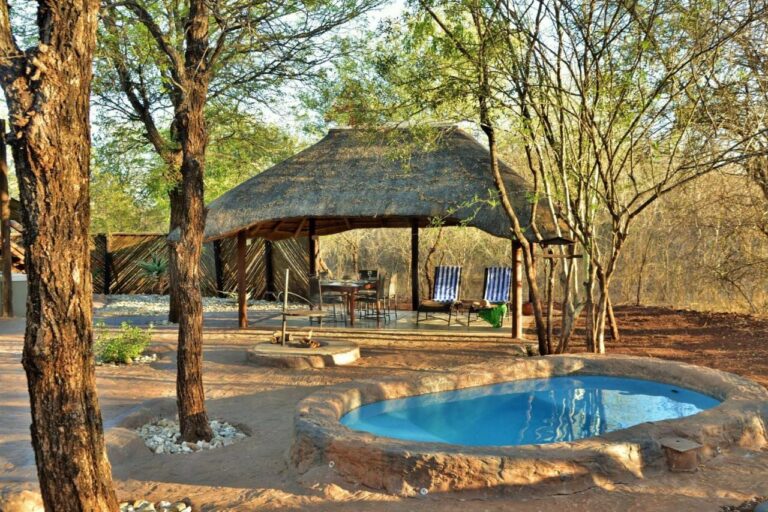 A round pool in front of a thatched shelter, with a dining table and two striped loungers
