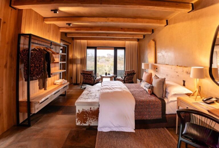 A suite with a double bed, a cowhide bench and an open wardrobe