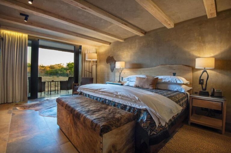 A suite with a double bed, a hide bench at the foot of the bed and a furnished terrace facing the bush