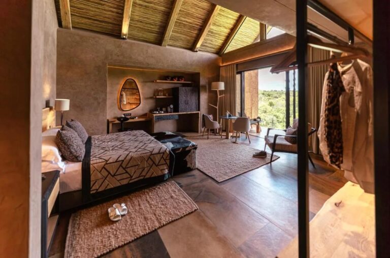 A suite at Kapama River Lodge under a wood and thatch roof frame, with a desk area and a view of the trees