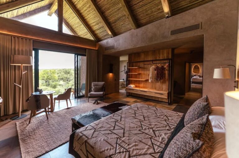 A suite under a high thatched roof, with a double bed, a small table and an open wardrobe