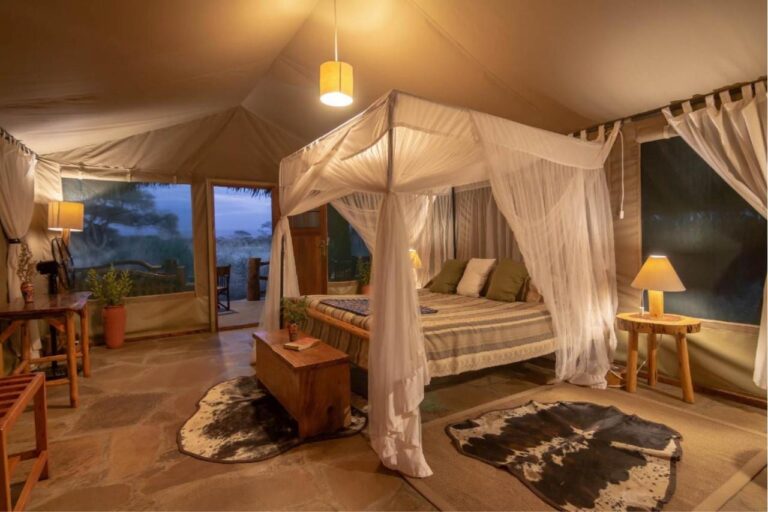 A four-poster bed under a mosquito net between two cowhides, in a tent lit up in the evening