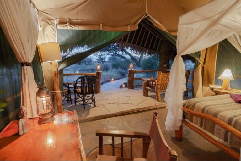 A tent's desk with a lantern, facing the thatched terrace and the bush