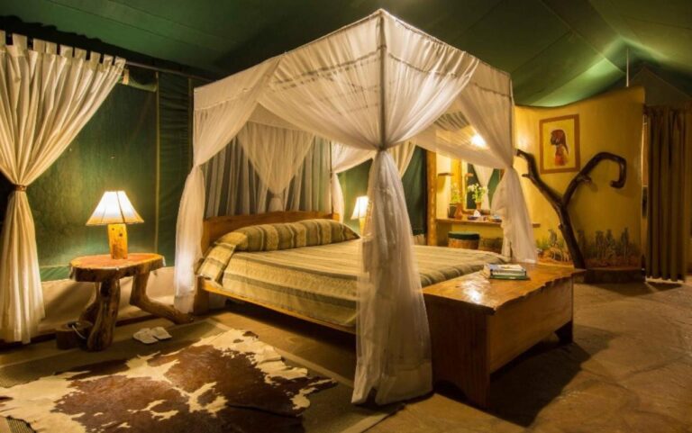 A tent with green canvas walls, a bed under a mosquito net and a framed portrait on a yellow partition