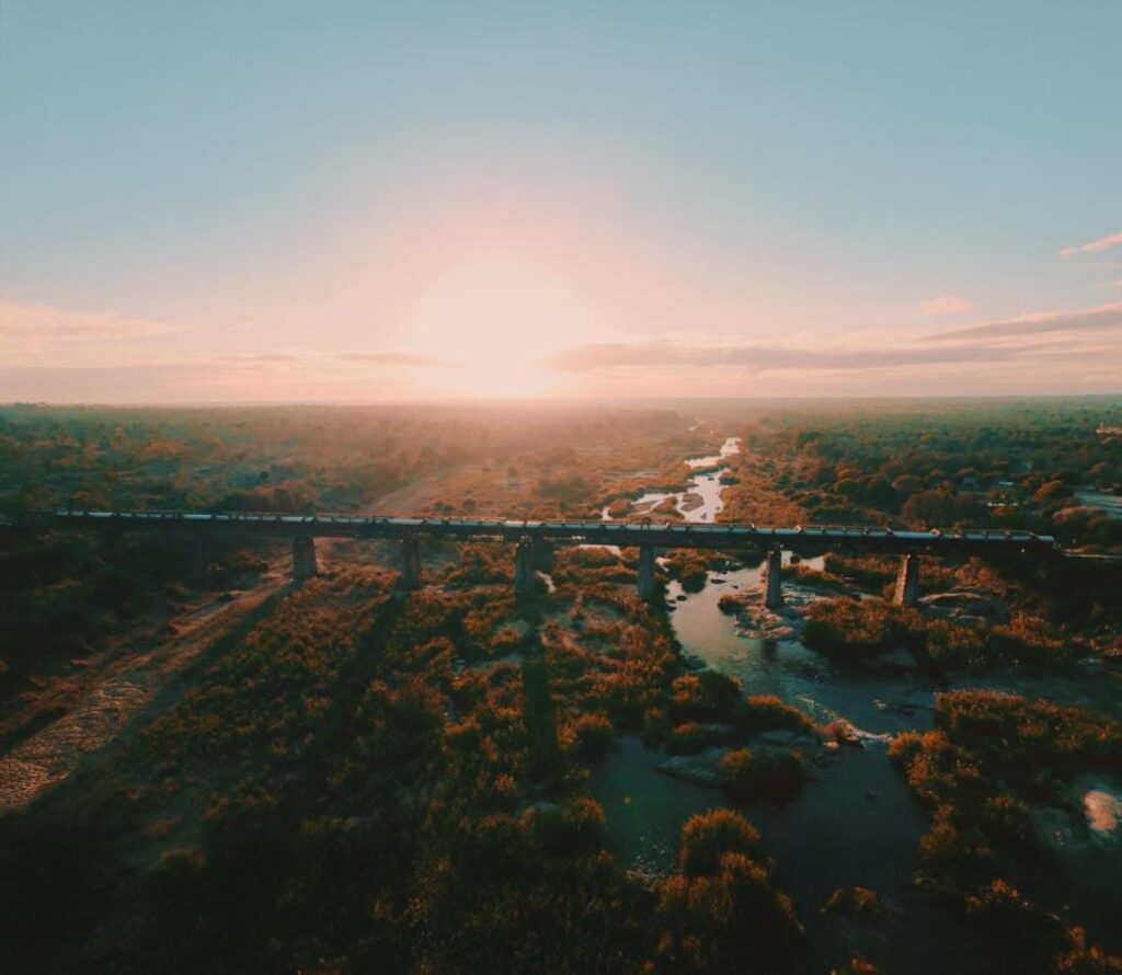 The Kruger Shalati train on the Selati Bridge, seen from the air, above the river and the bush, with the sun low on the horizon