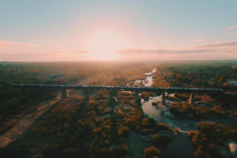The Kruger Shalati train on the Selati Bridge, seen from the air, above the river and the bush, with the sun low on the horizon