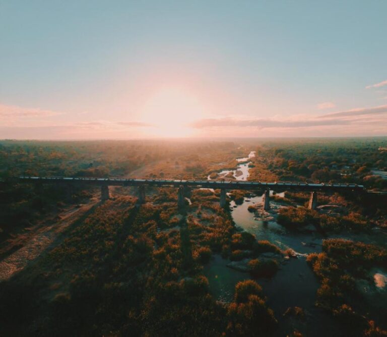 The Kruger Shalati train on the Selati Bridge, seen from the air, above the river and the bush, with the sun low on the horizon