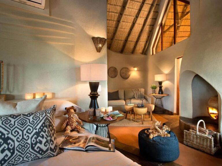Two soft-toy giraffes, on the bed and on a pouf, facing the seating area and its lit fireplace