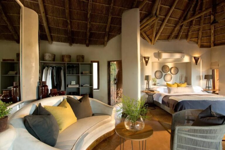 A suite at Madikwe Safari Lodge with a curved white sofa, a double bed and an open wardrobe