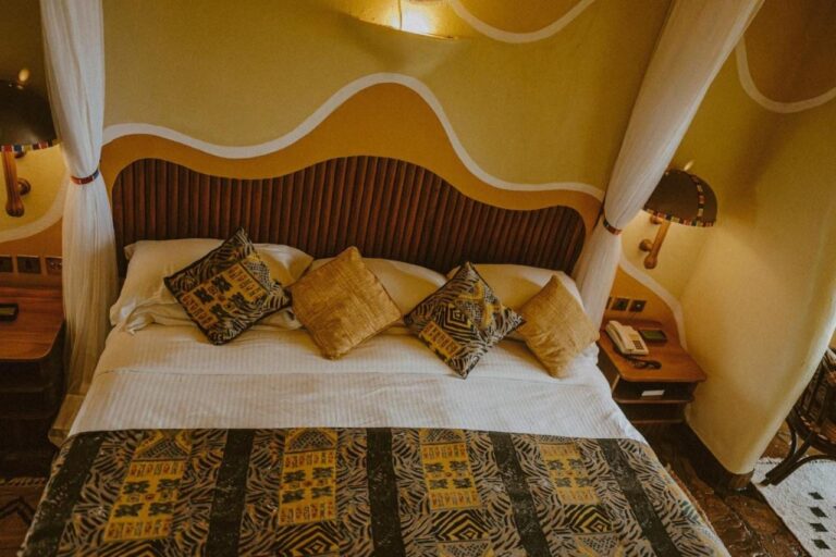 A large bed with African-patterned cushions, under a wooden slat headboard and walls painted in waves