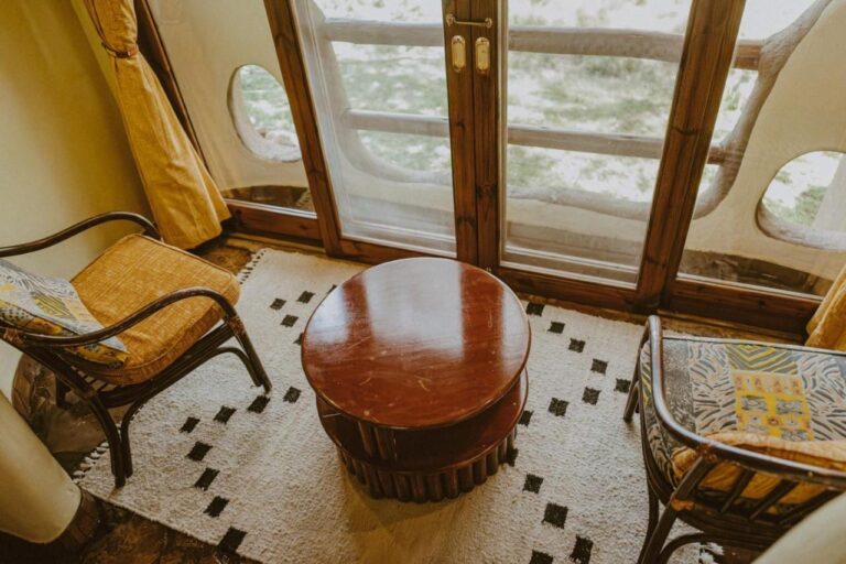 Two armchairs and a round table in front of a French door, with the savanna beyond the balcony railing