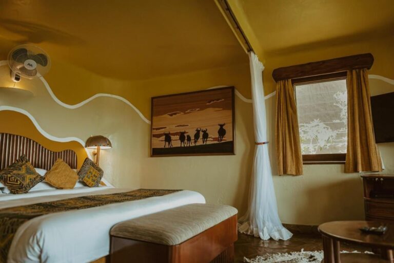 A room with a painting of wildebeest in silhouette above the bed and a wall fan