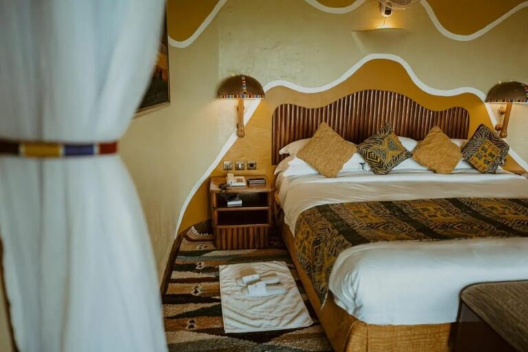 A large bed and slippers set on a towel, behind a sheer curtain held back by a band of beads
