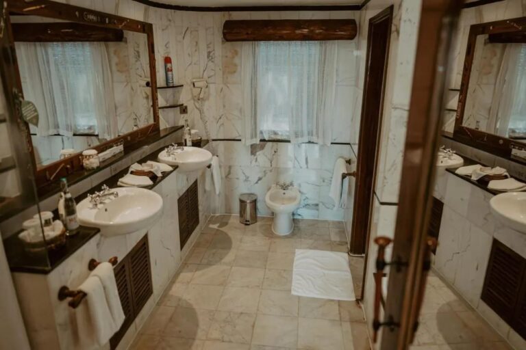A white marble bathroom, with two sinks, a wall-mounted hairdryer and a bidet under the window