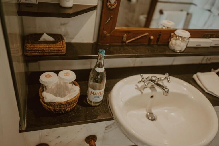 A sink with a bottle of water, cotton pads and a wicker tissue box