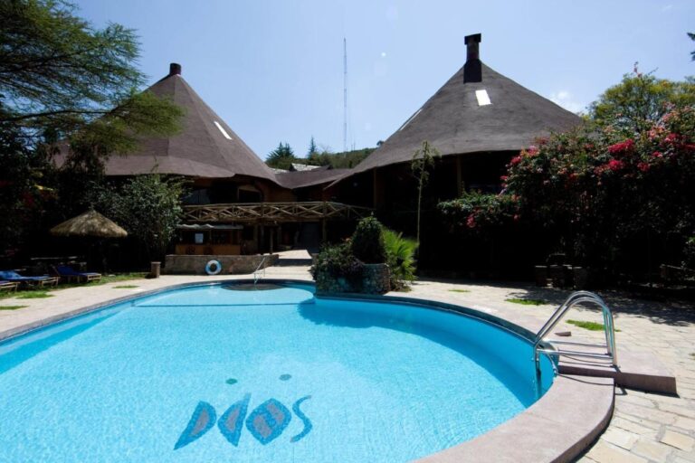 The pool at Mara Sopa Lodge, in front of buildings with tall conical thatched roofs
