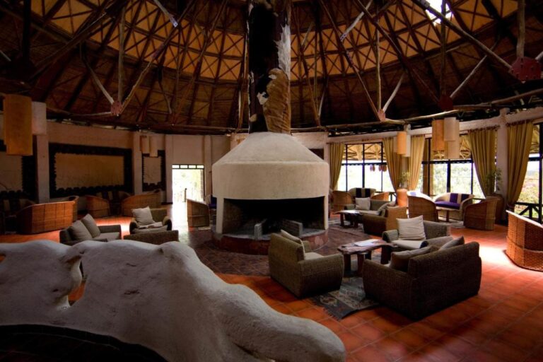 A lounge under a round wooden roof frame, with armchairs around a white fireplace