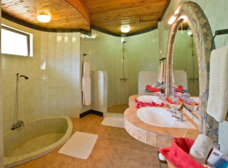 A green-tiled bathroom, with a round sunken shower tray and two basins under an arched mirror