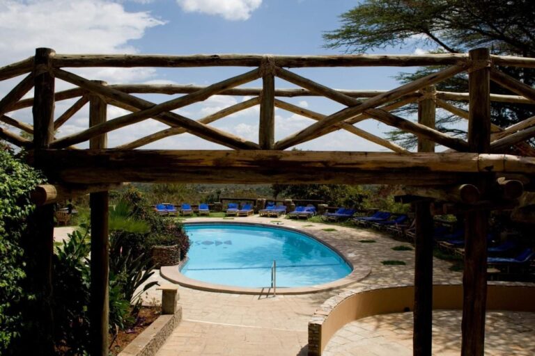 The pool seen through a log pergola, surrounded by sun loungers