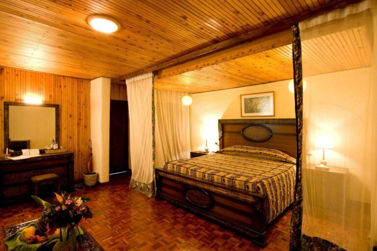 A room with a paneled ceiling, a large four-poster bed and a dressing table